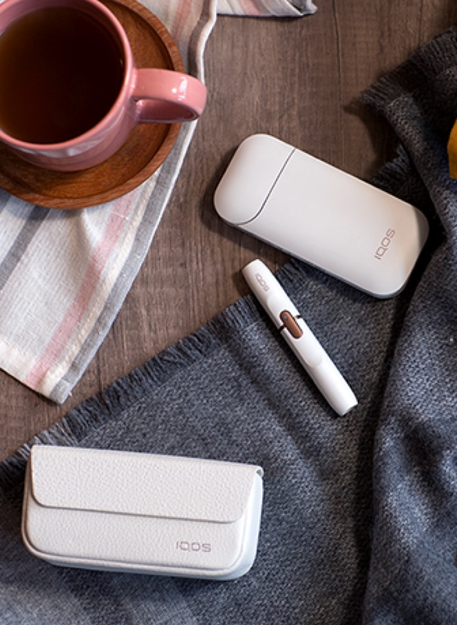 Two people talking at a table bar, one smokes IQOS and the other uses his phone